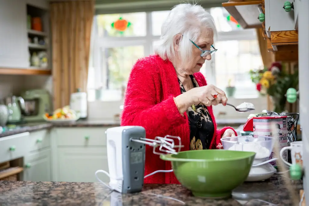 A woman in a red cardigan prepares food at her kitchen counter.
